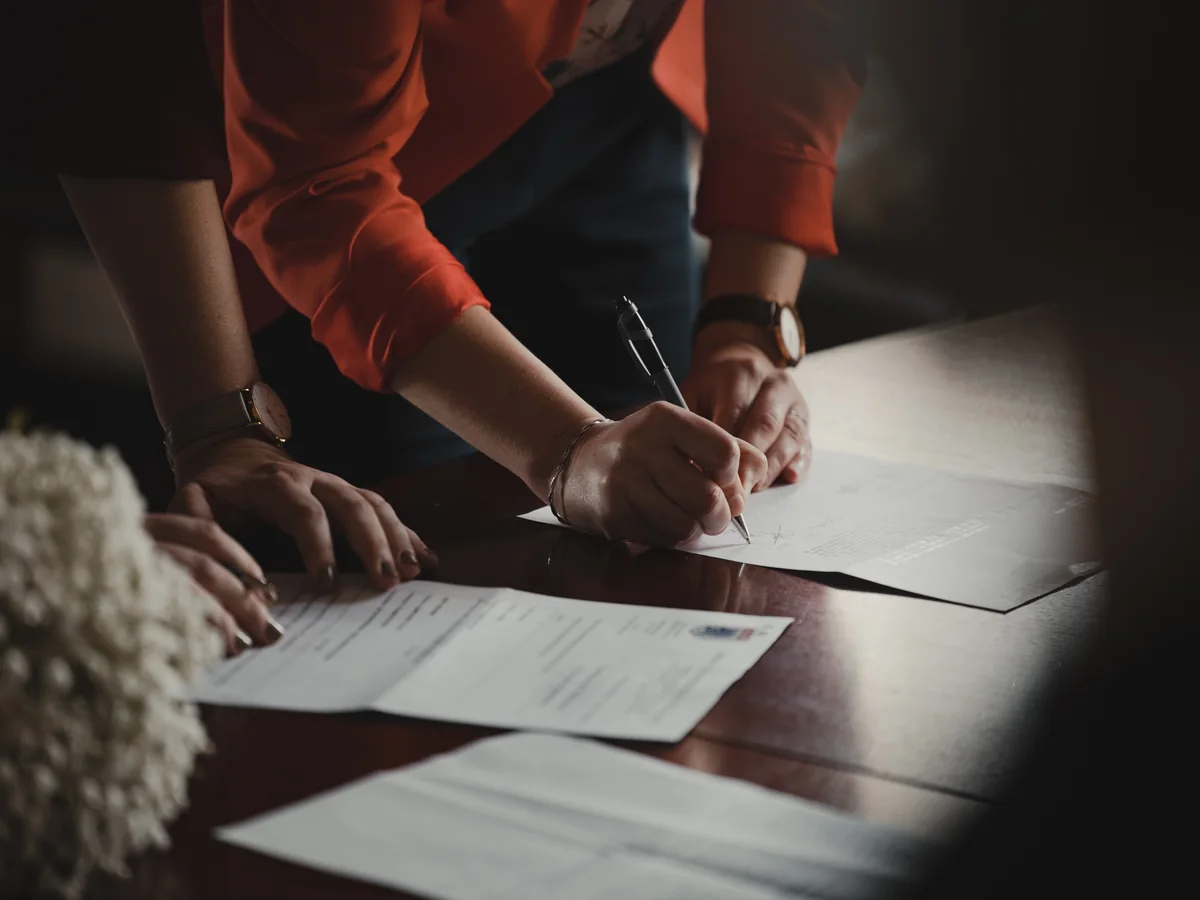Hands completing paper forms at a table.
